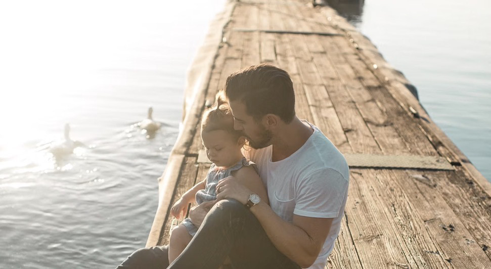 A parent holding a young child while sitting together beside the water